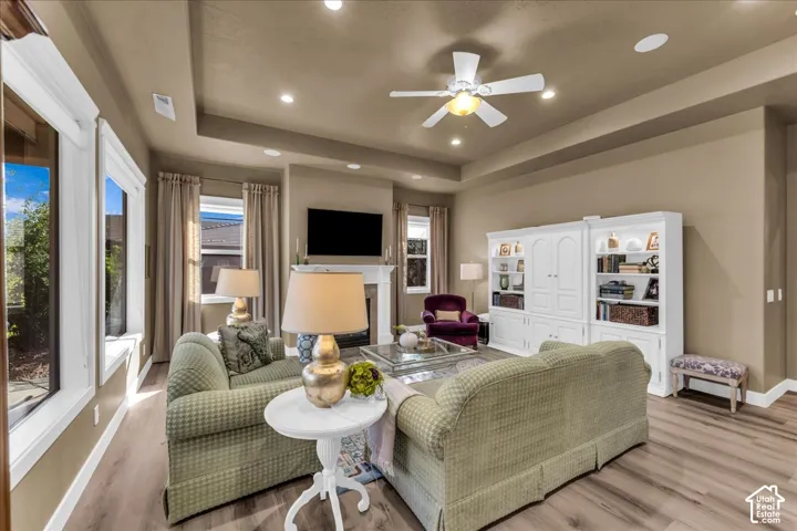 Tray ceiling with recessed lighting, wood-finish flooring, white fireplace surround, and multiple windows