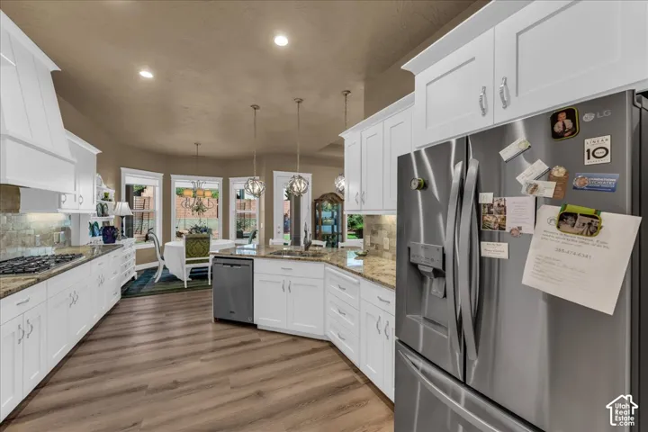 White cabinetry, stainless steel appliances, granite countertops, wood-finish flooring, and recessed lighting
