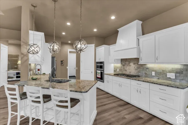 Kitchen featuring a large island with granite countertop, white cabinetry, integrated double oven, gas cooktop, and wood-finish flooring