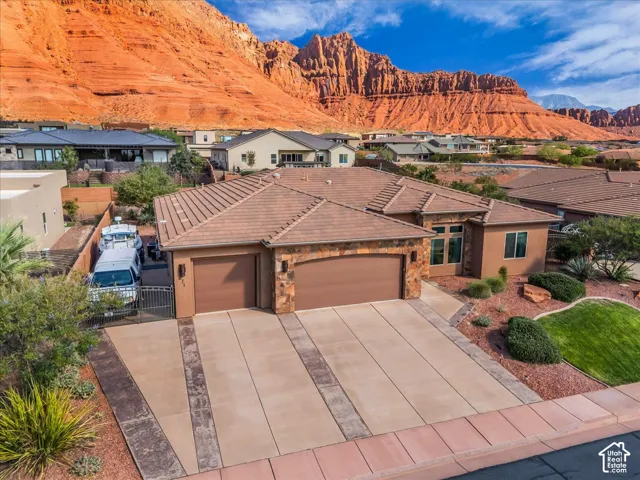 Stucco exterior with stone accents, concrete tile roof, two-car garage, established desert landscaping, and a red rock mountain backdrop