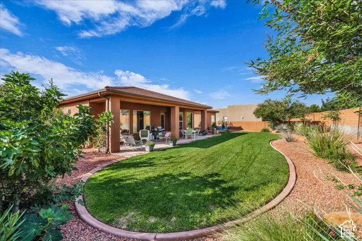 Expansive backyard featuring a manicured lawn, a covered patio, and desert-adapted landscaping with gravel pathways