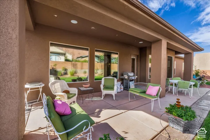 Covered patio with recessed lighting, stucco exterior, multiple large windows, and concrete hardscaping
