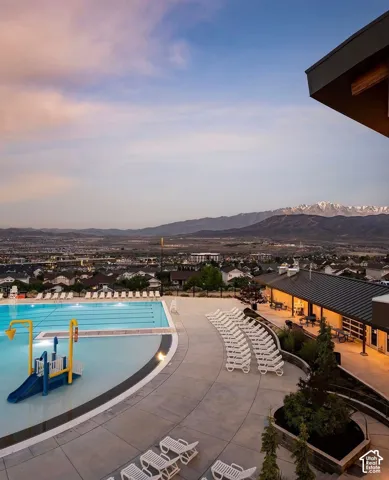 Swimming pool complex featuring a multi-lane lap area, integrated water feature, expansive concrete decking, and mountain range backdrop