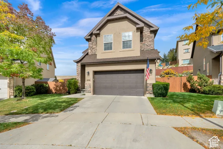 Two-story stucco exterior with stone accents, attached two-car garage, concrete driveway, and front lawn