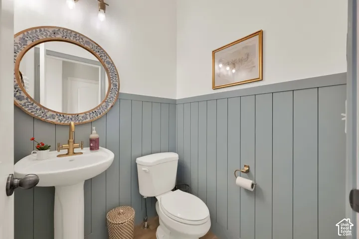 Pedestal sink with brass-finish faucet, elongated toilet, and wall-mounted board and batten paneling
