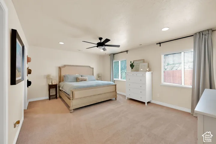 Recessed lighting, ceiling fan, two windows with blinds, and neutral carpet flooring