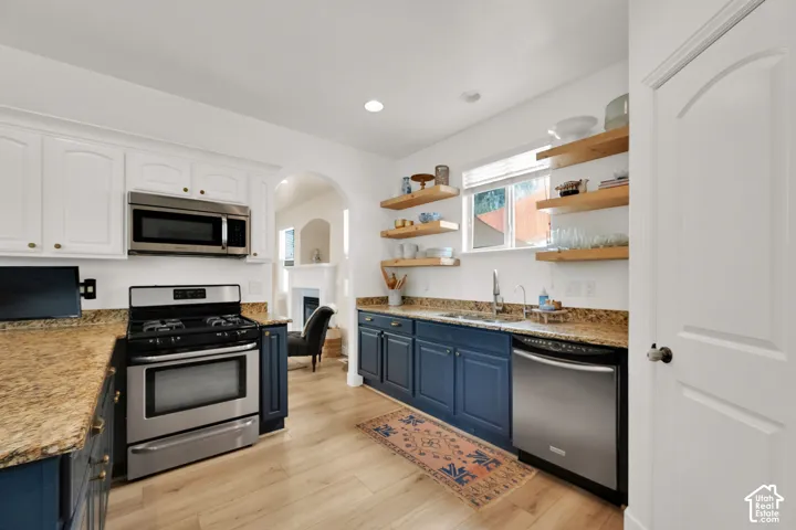 Kitchen featuring wood-finish flooring, stainless steel appliances, granite countertops, white upper cabinetry, and blue lower cabinetry