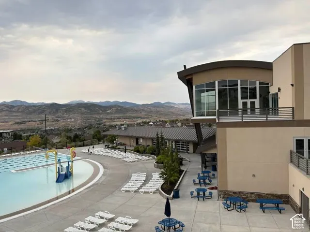 Multi-level community center featuring a swimming pool, concrete patio, metal roof, and metal balcony railings, set against a mountainous horizon