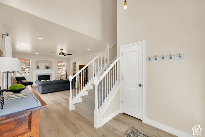 Spacious living area featuring high ceilings, recessed lighting, wood-finish flooring, a white mantel fireplace, and a ceiling fan