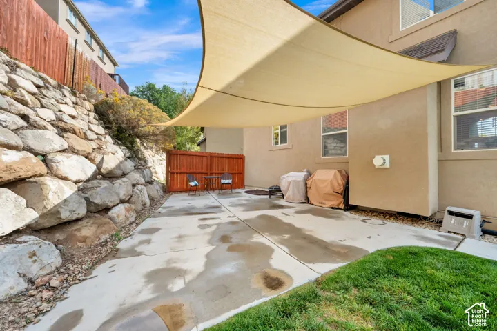 Paved patio space featuring a shade sail, rock retaining wall, and wood privacy fencing