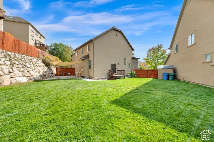 Expansive green lawn, wood fence, rock retaining wall, shade sail, and an exterior storage shed