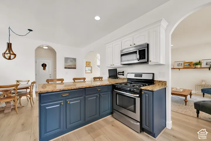 Kitchen featuring a gas range, stainless steel microwave, white upper cabinetry, blue lower cabinetry, and stone countertops