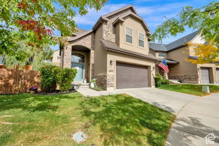 Stucco and stone exterior, arched entry, two-car garage, concrete driveway, and front lawn