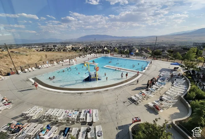 Community pool with a zero-entry basin, integrated water play structure, concrete decking, and mountain backdrop