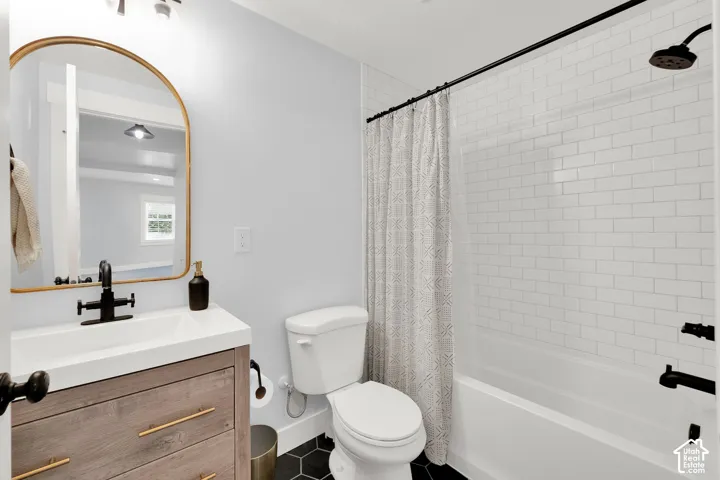 Bathroom featuring a vanity with wood-finish cabinetry and gold-tone hardware, a rectangular sink with a matte black faucet, a gold-framed arched mirror, and a tiled shower with subway-style wall tile and a matte black shower head