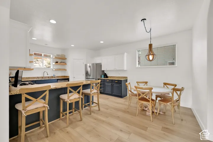 Open-concept kitchen featuring an island with seating, granite countertops, wood-finish flooring, white cabinetry, and stainless steel appliances