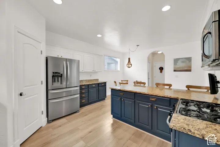 Kitchen featuring wood-finish flooring, two-tone cabinetry, stone countertops, recessed lighting, and an arched doorway