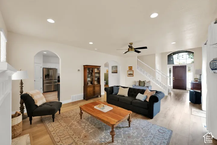 Open-concept living area with wood-finish flooring, recessed lighting, and a white staircase with a contrasting dark wood handrail