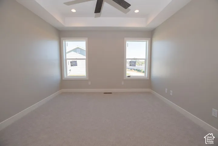 Tray ceiling with recessed lighting and a ceiling fan, neutral wall paint, two windows, and carpet flooring