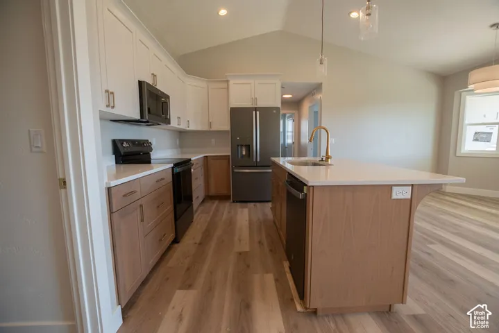 Kitchen featuring white upper cabinetry, wood-finish lower cabinetry, a center island with a sink and gold-tone faucet, and stainless-steel appliances