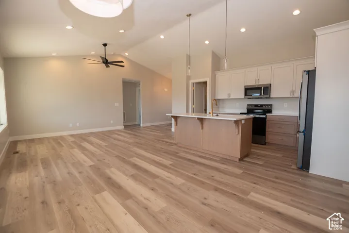 Vaulted ceilings with recessed lighting, wood-finish flooring, kitchen island with integrated sink, stainless steel appliances, and two-tone cabinetry