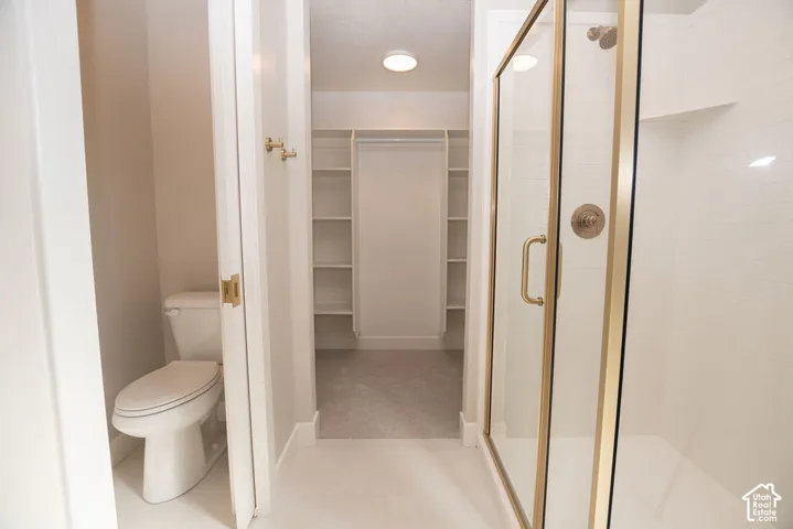 Recessed lighting, walk-in closet with built-in shelving, glass-enclosed shower with gold-tone fixtures, and a white subway tile shower surround