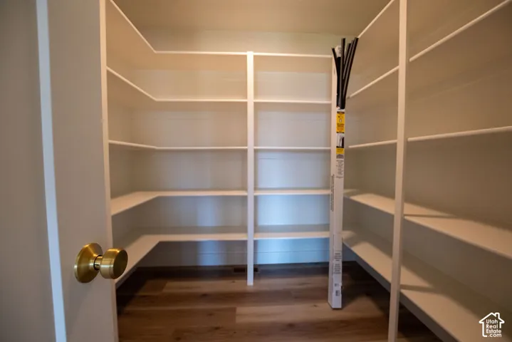 Walk-in pantry with extensive built-in shelving, wood-finish flooring, and a brass door knob
