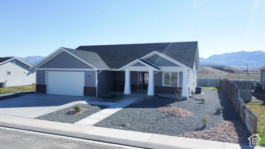 Single-story residence featuring a two-car garage, gray siding, stone veneer accents, covered entry, and a gravel-landscaped front yard