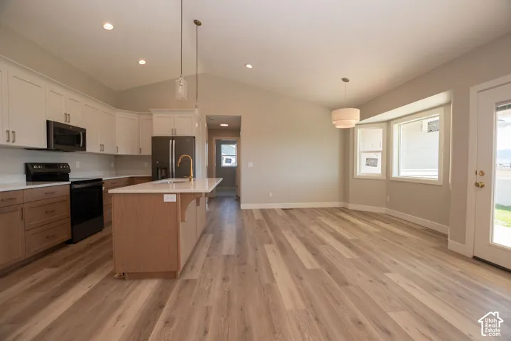 Open-concept kitchen and dining area featuring vaulted ceilings, wood-finish flooring, two-tone cabinetry, and a kitchen island with a gold-tone faucet