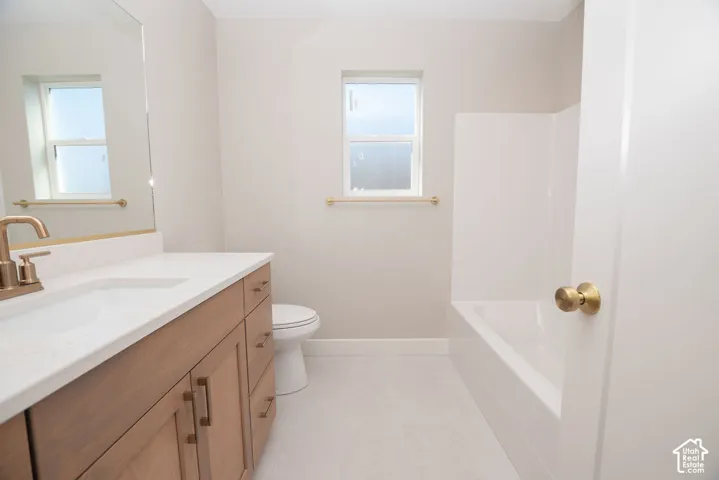 Wood-finish vanity with a white countertop and undermount sink, brushed gold hardware, and a white bathtub with a surrounding panel