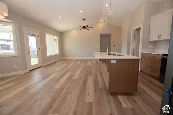 Open-concept living space with vaulted ceilings, recessed lighting, wood-finish flooring, and a kitchen island featuring a sink and gold-tone faucet
