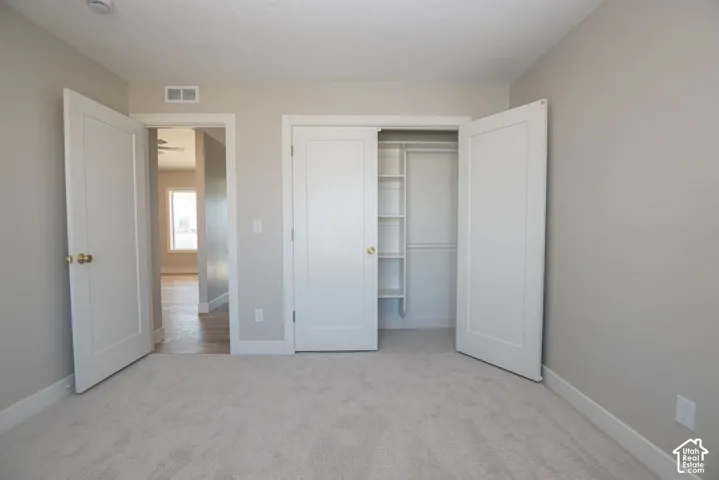 Neutral painted walls, light-colored carpet, and a closet with shelving and hanging rods