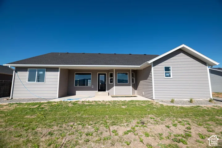 Back exterior featuring light gray siding, dark shingle roofing, multiple windows, and a concrete patio