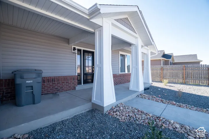 Covered entry with decorative pillars, gray siding, brick wainscoting, and a concrete pathway surrounded by decorative rock