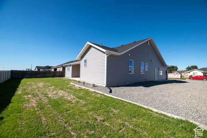 Exterior featuring gray horizontal siding, an asphalt shingle roof, white trim, and a gravel parking area