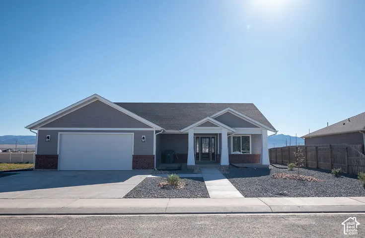 Contemporary exterior with gray siding, brick accents, attached garage, covered entry, and gravel landscaping
