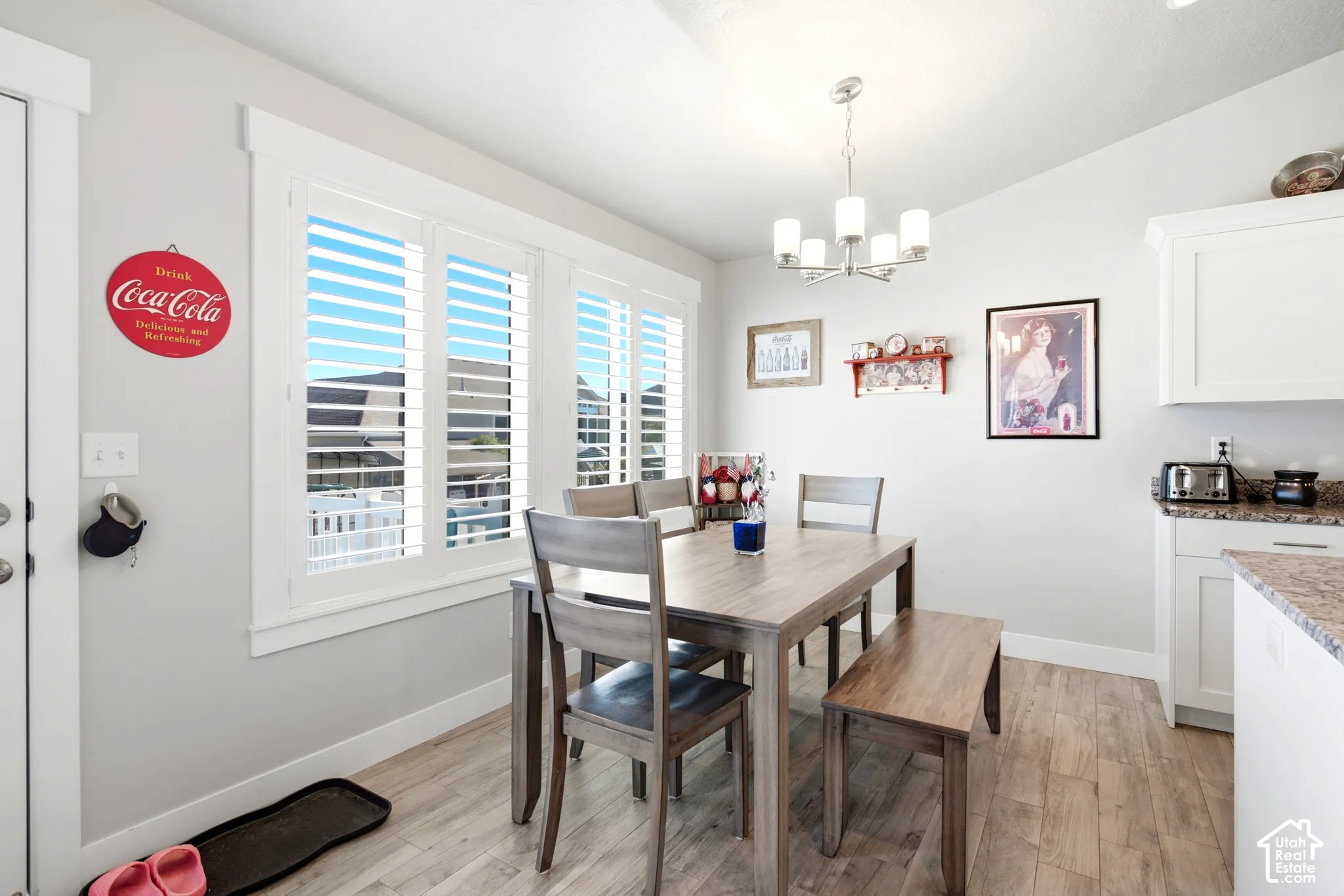 Dining area featuring extensive plantation shutters, wood-finish flooring, a modern chandelier, white cabinetry, and granite countertops