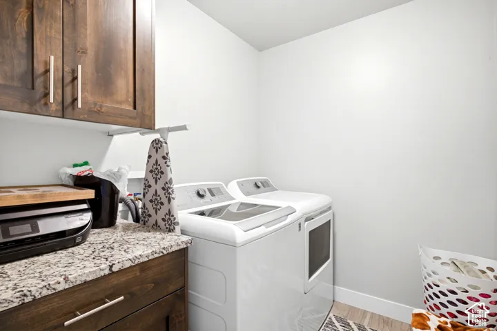 Dedicated laundry area featuring a white washer and dryer pair, custom wood cabinetry, and a light-toned speckled countertop