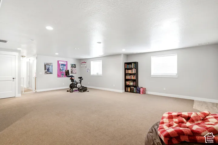 Expansive carpeted room featuring recessed lighting, a built-in bookshelf, and multiple windows with blinds