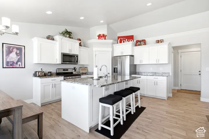 Bright kitchen featuring an expansive center island with seating, white cabinetry, stainless steel appliances, granite countertops, and wood-finish flooring