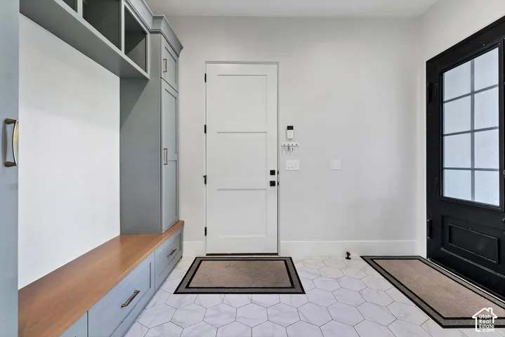 Built-in cabinetry with wood-finish bench, hexagonal floor tiling, and a black paneled door with frosted glass
