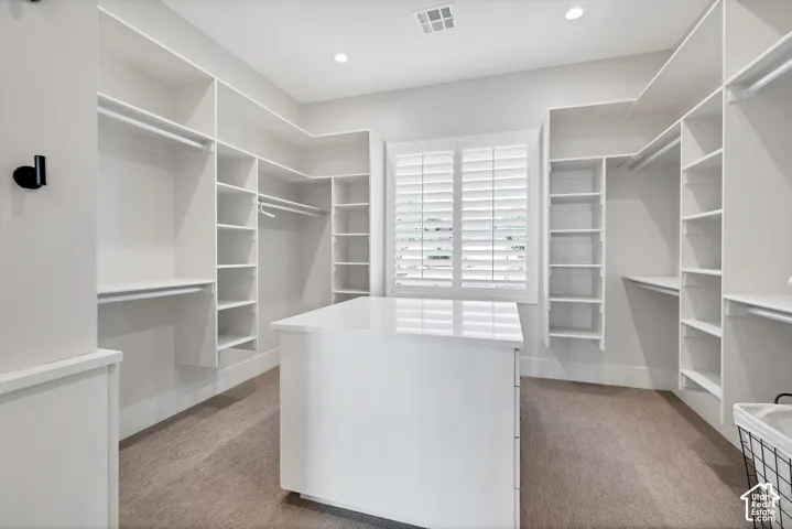 Expansive custom closet featuring ample built-in shelving, hanging rods, central storage island, and plantation shutters