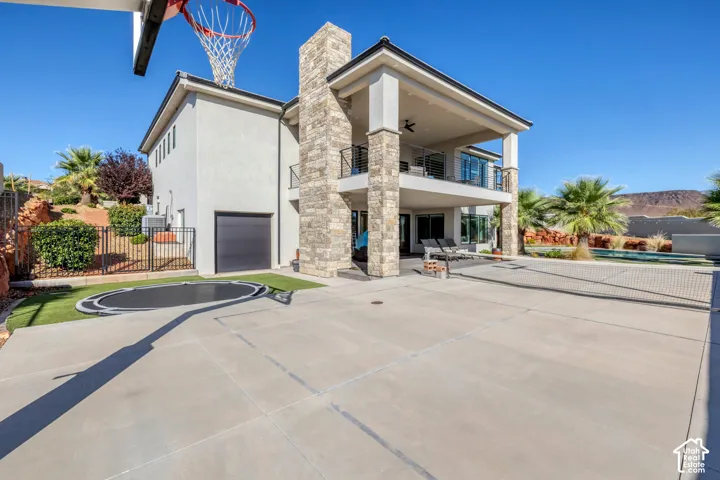 Stucco exterior with stone accents, covered patio, upper-level balcony, built-in trampoline, and expansive concrete hardscaping