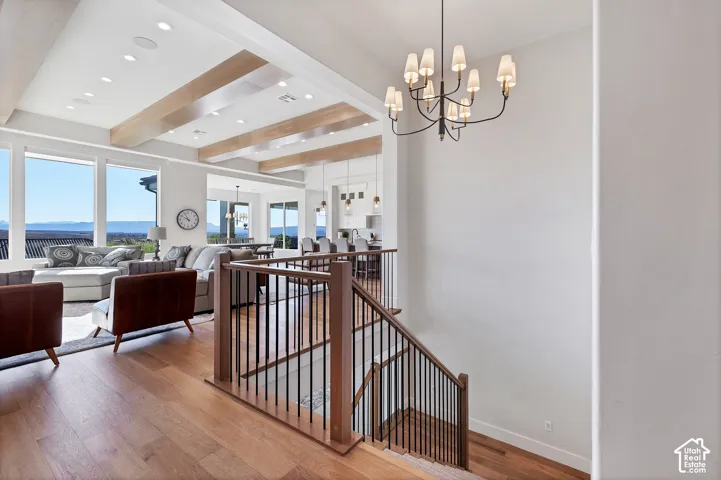 Wood-finish flooring, staircase with wood newel posts and metal balusters, exposed wood ceiling beams, recessed lighting, and a multi-arm chandelier