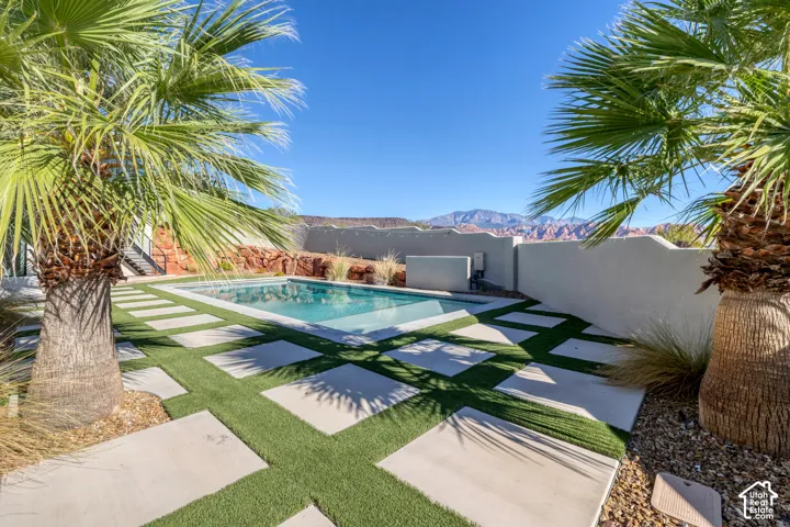 Outdoor swimming pool surrounded by concrete pavers and artificial turf, featuring palm trees and a perimeter wall