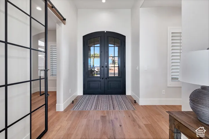 Arch-top double entry doors, wood-finish flooring, white plantation shutters, and a black-framed glass barn door