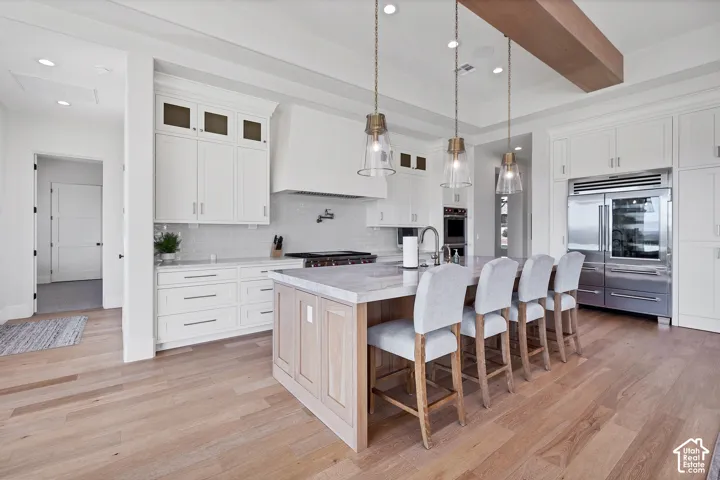 White cabinetry with glass-front upper cabinets, light wood-finish flooring, and a large central island with seating