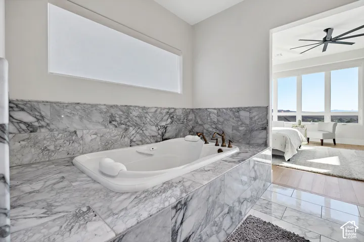 Built-in soaking tub with marble surround, bronzed fixtures, and a horizontal window with a privacy shade