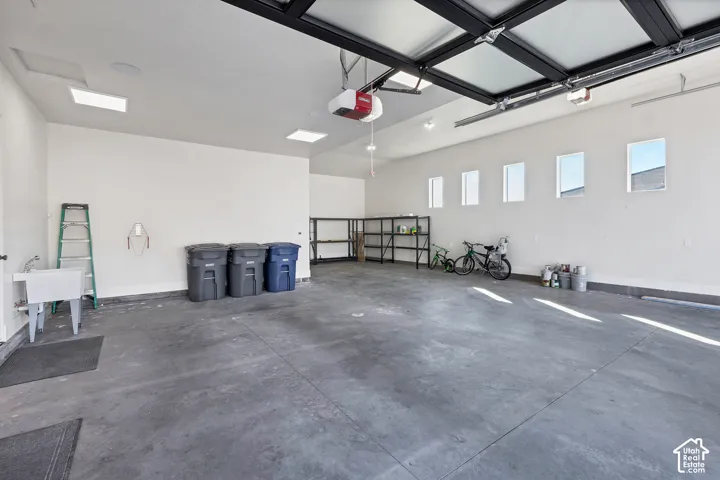 Spacious garage featuring a finished concrete floor, utility sink, five transom windows, and overhead lighting