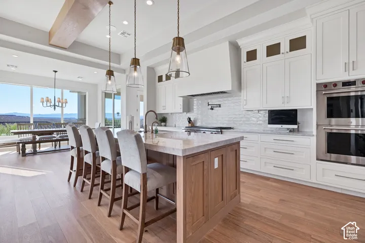 Gourmet kitchen featuring a wood-panel island with stone countertop, white cabinetry, stainless steel double ovens, and wood-finish flooring